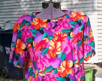 Könnte beinhalten: Eine kurzärmelige Bluse mit floralem Druck in Rosa, Lila, Orange und Grün mit einem runden Ausschnitt.