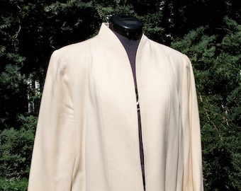 May include: A cream-colored blazer with a long, open collar and two pockets. The blazer is made of a soft, textured fabric.