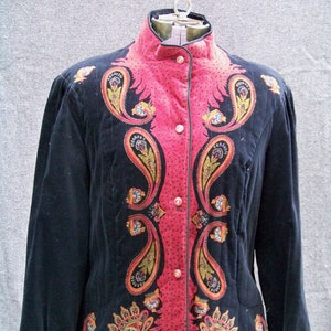 Puede incluir: Una chaqueta de terciopelo negro con un estampado paisley rosa. La chaqueta tiene un cuello alto y cierre de botones.