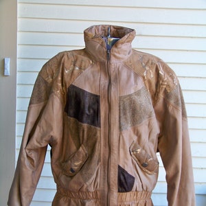 May include: A brown leather jacket with a zipper closure and a patchwork design. The jacket has a stand-up collar and a ribbed waistband.