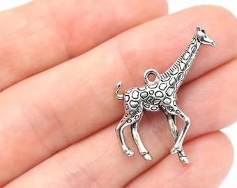 May include: A silver-colored giraffe charm with a textured coat pattern and a loop for attaching to jewelry or other crafts. The giraffe is depicted in a walking pose, with detailed legs and a long neck.