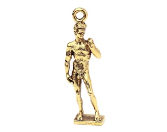 May include: A small, gold-colored statue of a nude male figure, likely a classical sculpture. The figure stands on a rectangular base and has a loop at the top for hanging. The statue is detailed and has a textured surface.