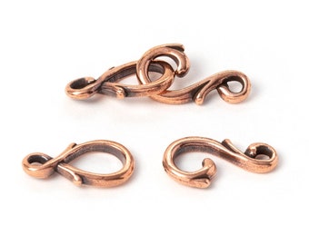 May include: Three antique copper-colored clasps with an ornate, swirling design. The clasps are in various positions, with one connected and two separate, all against a white background. These are likely jewelry findings.
