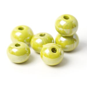 May include: Six round, pale green ceramic beads with a shiny finish. Each bead has a hole through the centre. The beads are arranged on a white background, with some stacked on top of each other.