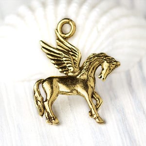 Op de afbeelding: Een goudkleurige Pegasus-bedel met gedetailleerde vleugels en een lus om aan sieraden of andere knutselwerkjes te bevestigen. Het mythische gevleugelde paard wordt in profiel afgebeeld, met het hoofd omhoog.