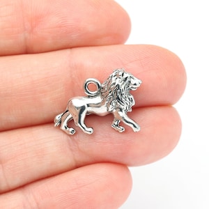 Op de afbeelding: Een kleine, zilverkleurige leeuwenbedel met gedetailleerde manen en lichaam. De leeuw wordt afgebeeld in een loopstand, met een lus aan de bovenkant om aan een ketting of armband te bevestigen. De bedel is waarschijnlijk van metaal.
