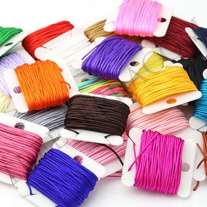 Puede incluir: Una colecci&oacute;n de coloridas bobinas de cord&oacute;n en varios tonos, incluyendo verde, rojo, blanco, naranja, morado, marr&oacute;n, amarillo, rosa, azul y negro. Los cordones est&aacute;n cuidadosamente enrollados en bobinas de cart&oacute;n blanco, creando una exhibici&oacute;n vibrante y organizada.