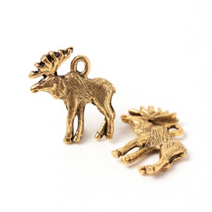 Op de afbeelding: Twee bronzen elandbedels. Eén eland staat, de andere ligt. Beide bedels hebben gedetailleerde geweien en een lus om aan sieraden of knutselwerk te bevestigen. De bedels staan op een witte achtergrond.