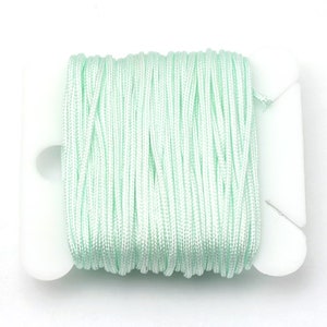 Puede incluir: Un carrete de cord&oacute;n verde menta est&aacute; cuidadosamente enrollado en un soporte de pl&aacute;stico blanco. El cord&oacute;n parece estar hecho de un material liso, posiblemente sint&eacute;tico. Fondo blanco.