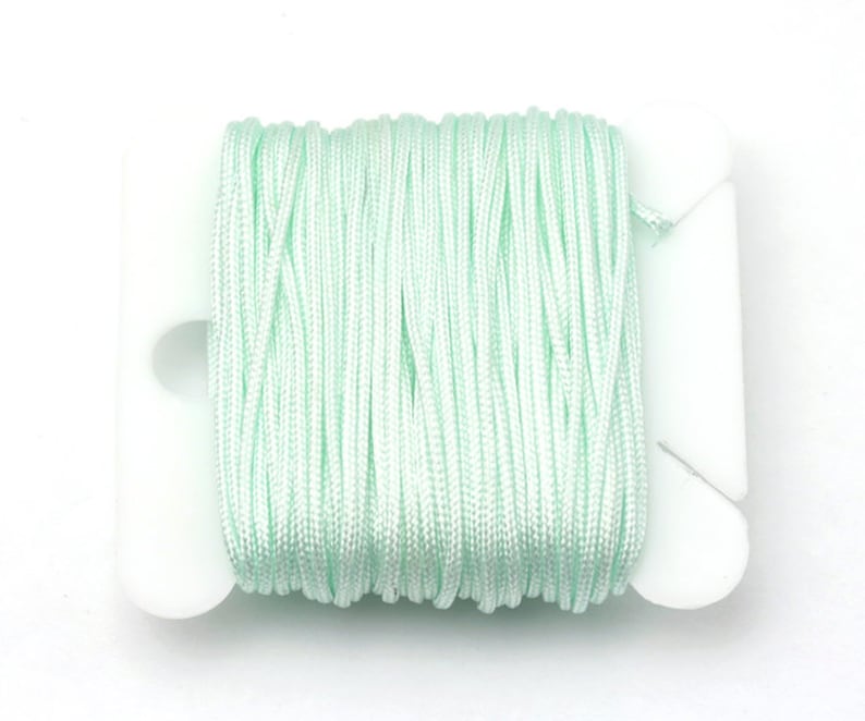 Puede incluir: Un carrete de cord&oacute;n verde menta est&aacute; cuidadosamente enrollado en un soporte de pl&aacute;stico blanco. El cord&oacute;n parece estar hecho de un material liso, posiblemente sint&eacute;tico. Fondo blanco.