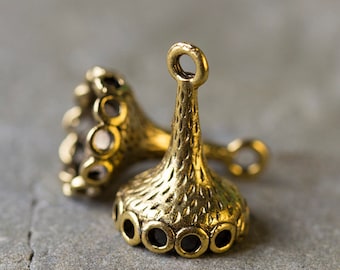 May include: Two gold-colored metal charms. Each charm has a bell-like shape with a textured surface and a small loop at the top. The base of each charm has several circular openings. These charms are suitable for jewelry making.