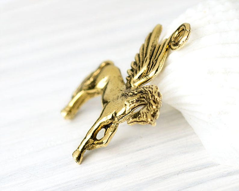 Op de afbeelding: Een gedetailleerde, antiek goudkleurige Pegasus bedel. Het mythische gevleugelde paard is afgebeeld in een dynamische pose, met uitgestrekte vleugels en een vloeiende manen. De bedel heeft een lus aan de bovenkant voor bevestiging.