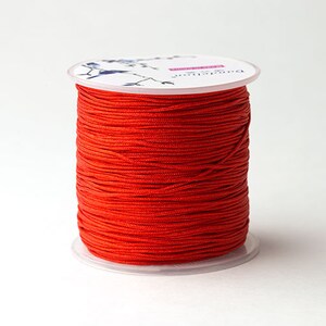 Puede incluir: Una bobina de hilo rojo brillante, bien enrollado, con una base de pl&aacute;stico transparente y una parte superior blanca. La parte superior de la bobina tiene un dise&ntilde;o floral y la palabra "Dandelion" impresa. El hilo es de color s&oacute;lido.