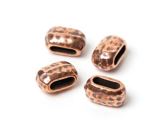 May include: Four copper-colored, hammered-finish oval beads with a dark interior. The beads are scattered on a white background. The beads have a rustic, vintage appearance, suitable for jewelry making or craft projects.