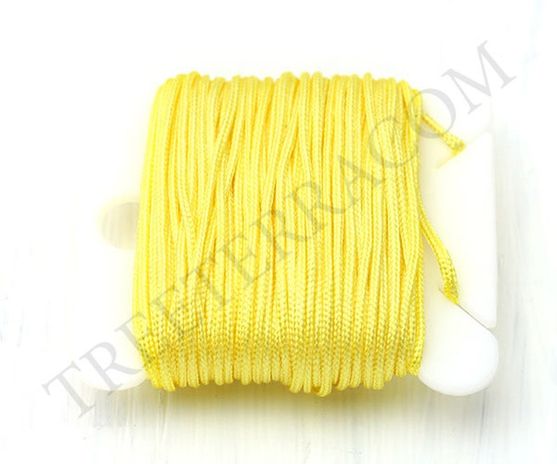 Puede incluir: Un carrete de cord&oacute;n amarillo brillante, bien enrollado. El cord&oacute;n es de un color amarillo vibrante y soleado, y est&aacute; enrollado en un soporte de pl&aacute;stico blanco. La imagen est&aacute; tomada sobre un fondo blanco.
