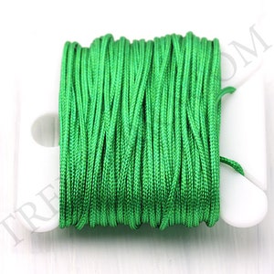 Puede incluir: Un carrete de hilo de nailon verde brillante. El hilo est&aacute; enrollado firmemente en una bobina de pl&aacute;stico blanco. La imagen es un primer plano que resalta la textura y el color del hilo. El hilo parece nuevo y sin usar.