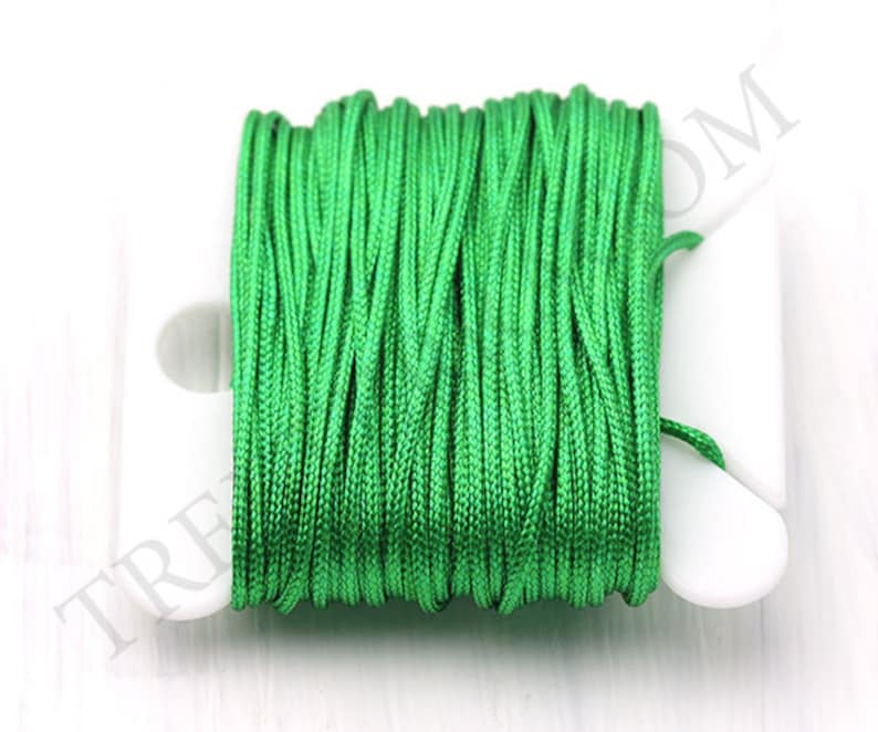 Puede incluir: Un carrete de hilo de nailon verde brillante. El hilo est&aacute; enrollado firmemente en una bobina de pl&aacute;stico blanco. La imagen es un primer plano que resalta la textura y el color del hilo. El hilo parece nuevo y sin usar.