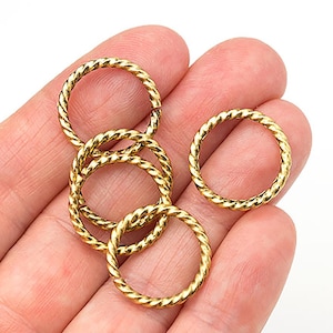 May include: Close-up of several gold-colored, twisted metal rings. The rings are circular and have a textured, rope-like appearance. The rings are displayed on a light-colored surface.