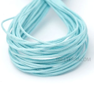 May include: Close-up of a bundle of light blue waxed cotton cord. The cord is tightly wound, revealing the texture of the individual strands. The color is a soft, pastel blue, suitable for various crafting projects.