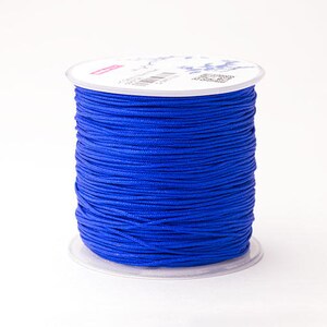 Puede incluir: Un carrete de cord&oacute;n azul vibrante, bien enrollado y listo para manualidades. El cord&oacute;n es de un azul rico y saturado, y el carrete se asienta sobre una base de pl&aacute;stico transparente. La parte superior del carrete tiene una etiqueta blanca con texto y un dise&ntilde;o.