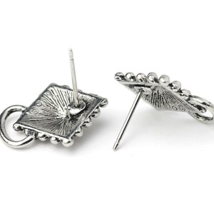 May include: Two silver-toned stud earrings. Each earring features a square design with a beaded border and a small loop. The earrings have a vintage, antique appearance, with a post for piercing.