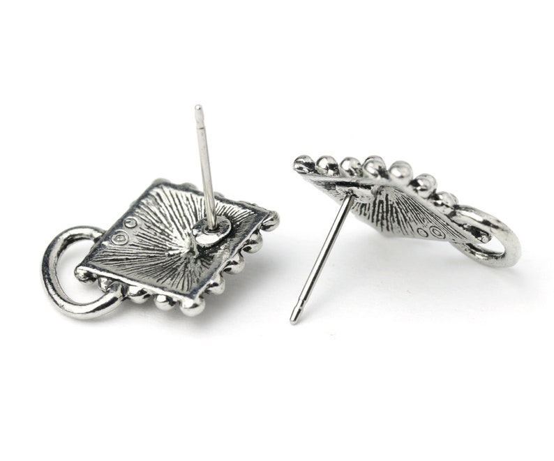 May include: Two silver-toned stud earrings. Each earring features a square design with a beaded border and a small loop. The earrings have a vintage, antique appearance, with a post for piercing.