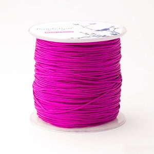 Puede incluir: Un carrete de cord&oacute;n magenta vibrante. El cord&oacute;n est&aacute; enrollado alrededor de una bobina de pl&aacute;stico transparente. La parte superior de la bobina tiene una etiqueta blanca con el nombre de la marca "Dandelion" y un dise&ntilde;o decorativo de p&aacute;jaro. El cord&oacute;n parece liso y es adecuado para manualidades.