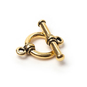 Può includere: Chiusura a toggle color oro, composta da un anello circolare e da una barra cilindrica. La chiusura ha una finitura anticata ed è progettata per la creazione di gioielli. La barra è lunga circa 1,9 cm.