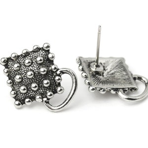 May include: Silver stud earrings with a textured, dotted design. Each earring has a square shape with a small handle and a post for piercing. The earrings have a vintage or antique aesthetic.