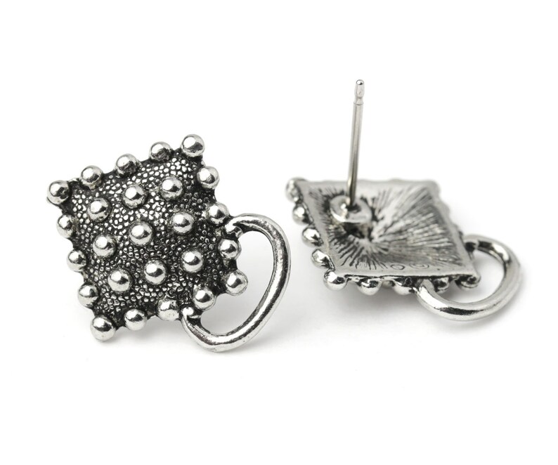 May include: Silver-toned stud earrings with a textured, dotted design. Each earring features a square shape with a small handle and a post for piercing. The earrings have a vintage or antique aesthetic.