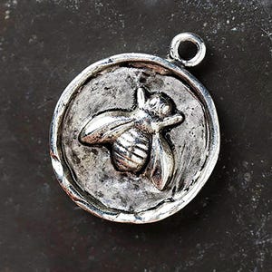 Peut inclure: Pendentif rond argenté avec un motif d'abeille en relief. L'abeille est centrée dans un cadre circulaire, et le pendentif a une boucle en haut pour l'attacher à une chaîne. Le pendentif a un aspect rustique et antique.