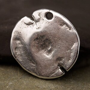 May include: A silver-colored, irregularly shaped pendant with a textured surface and a small hole at the top. The pendant has a split on one side, giving it a unique, rustic appearance. Ideal for jewelry making.