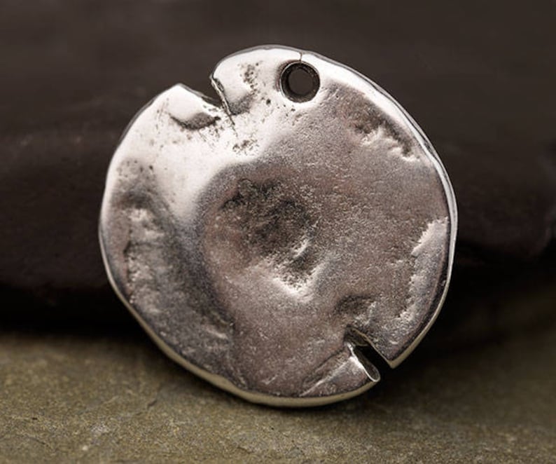 May include: A silver-colored, irregularly shaped pendant with a textured surface and a small hole at the top. The pendant has a split on one side, giving it a unique, rustic appearance. Ideal for jewelry making.