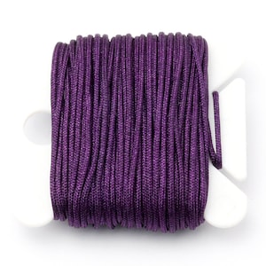 Puede incluir: Un carrete de cord&oacute;n morado oscuro, bien enrollado y exhibido en un soporte de pl&aacute;stico blanco. El cord&oacute;n tiene una textura suave y ligeramente brillante, lo que sugiere que est&aacute; hecho de un material sint&eacute;tico. El soporte blanco proporciona un contraste limpio con el rico color del cord&oacute;n.