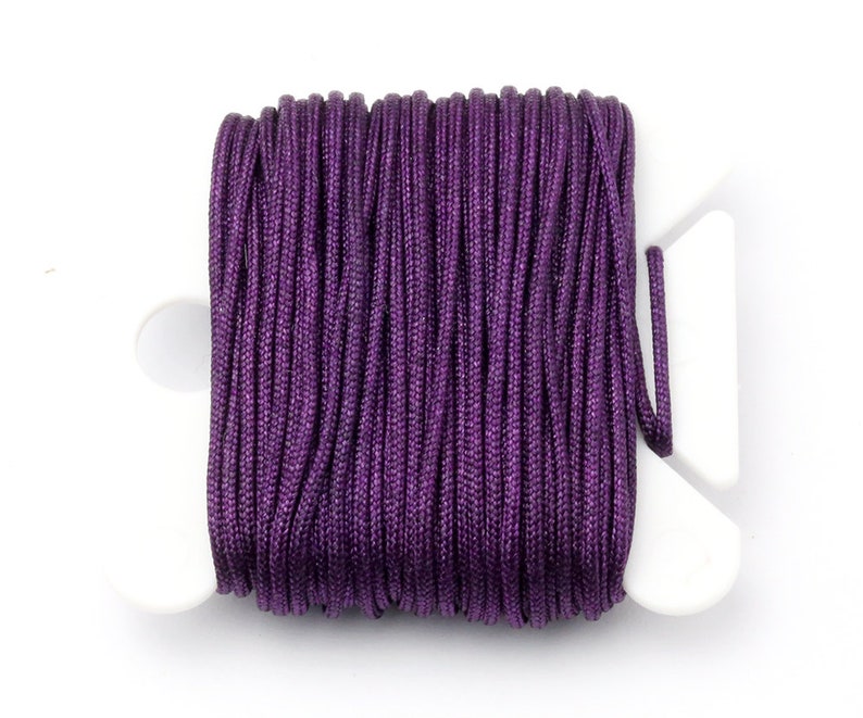 Puede incluir: Un carrete de cord&oacute;n morado oscuro, bien enrollado y exhibido en un soporte de pl&aacute;stico blanco. El cord&oacute;n tiene una textura suave y ligeramente brillante, lo que sugiere que est&aacute; hecho de un material sint&eacute;tico. El soporte blanco proporciona un contraste limpio con el rico color del cord&oacute;n.