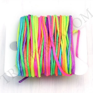 Puede incluir: Un carrete de cord&oacute;n colorido en tonos rosa, morado, verde, amarillo y naranja. El cord&oacute;n est&aacute; enrollado firmemente en un carrete de pl&aacute;stico blanco. Los colores brillantes crean una exhibici&oacute;n vibrante y llamativa.