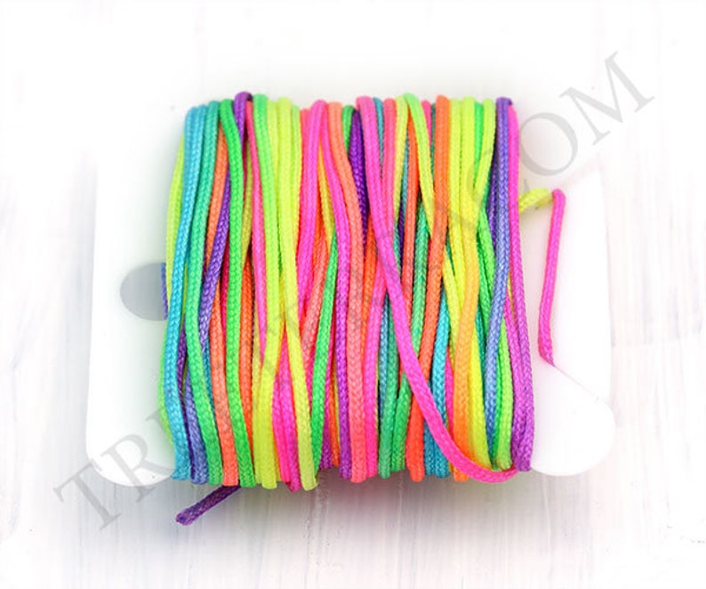 Puede incluir: Un carrete de cord&oacute;n colorido en tonos rosa, morado, verde, amarillo y naranja. El cord&oacute;n est&aacute; enrollado firmemente en un carrete de pl&aacute;stico blanco. Los colores brillantes crean una exhibici&oacute;n vibrante y llamativa.