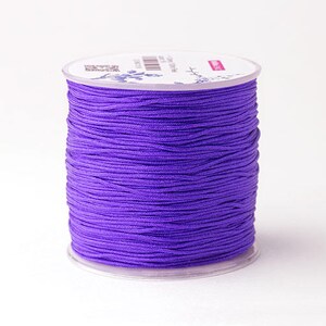 Puede incluir: Un carrete de cord&oacute;n morado vibrante, bien enrollado y exhibido sobre una base de pl&aacute;stico transparente. El cord&oacute;n parece liso y es adecuado para varios proyectos de manualidades. El carrete se encuentra sobre un fondo blanco liso.