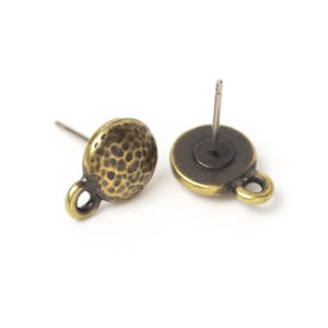 May include: Two antique brass-colored stud earrings with a textured, hammered surface. Each earring has a post for piercing and a small loop at the bottom. The earrings are set against a white background.