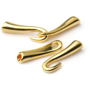 May include: Four gold-colored metal clasps, each with a curved hook shape. Two clasps are interlocked, while the other two are separate. One clasp has a small hole. The clasps are on a white background.