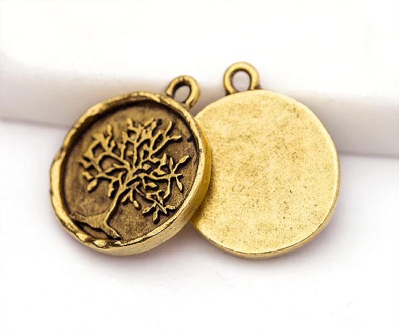 May include: Two antique gold-colored round pendants. One pendant features a detailed tree design, while the other has a plain surface. Both pendants have a small loop at the top for attaching to a chain or other jewelry.