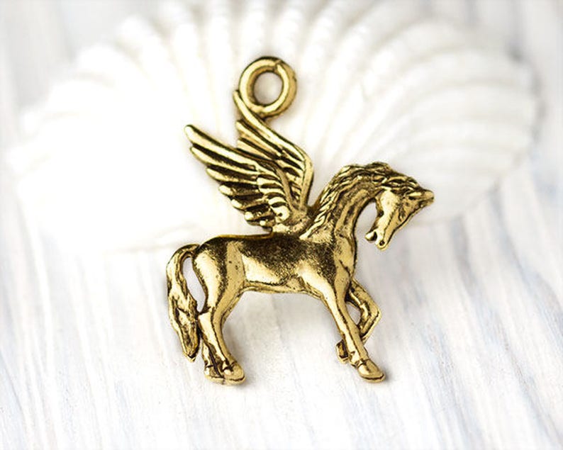 Op de afbeelding: Een goudkleurige Pegasus-bedel met gedetailleerde vleugels en een lus om aan sieraden of andere knutselwerkjes te bevestigen. Het mythische gevleugelde paard wordt in profiel afgebeeld, met het hoofd omhoog.