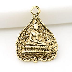 May include: A gold-coloured pendant depicting a seated Buddha within a leaf-shaped frame. The pendant has a loop at the top for hanging and detailed patterns on the leaf and Buddha's robes. The design is ornate and detailed, suitable for jewellery.