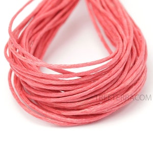 May include: Close-up of a spool of coral-colored waxed cotton cord. The cord is tightly wound, revealing multiple layers of the material. The texture of the cord is visible, and the color is consistent throughout the spool. The background is white.