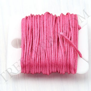 Puede incluir: Un carrete de cord&oacute;n rosa brillante, bien enrollado en un soporte de pl&aacute;stico blanco. El cord&oacute;n parece estar hecho de un material liso, posiblemente sint&eacute;tico. El fondo es una superficie blanca lisa, que resalta el color vibrante del cord&oacute;n.