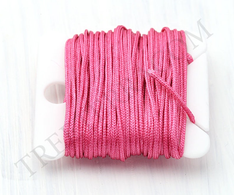 Puede incluir: Un carrete de cord&oacute;n rosa brillante, bien enrollado en un soporte de pl&aacute;stico blanco. El cord&oacute;n parece estar hecho de un material liso, posiblemente sint&eacute;tico. El fondo es una superficie blanca lisa, que resalta el color vibrante del cord&oacute;n.