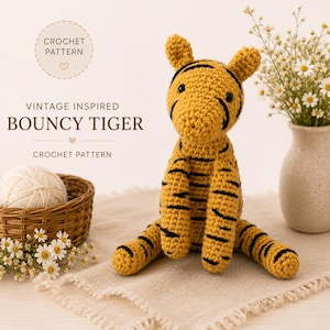 May include: A yellow and black crocheted tiger toy with pointed ears and black stripes. Text on the image reads: CROCHET PATTERN, VINTAGE INSPIRED BOUNCY TIGER, CROCHET PATTERN. The tiger is positioned next to a small woven basket with yarn.