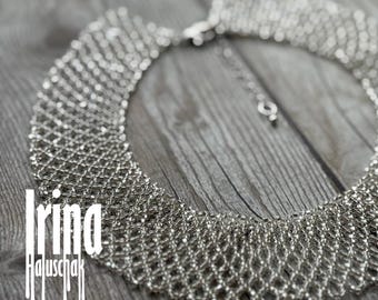 May include: A silver-toned statement necklace with a woven, mesh-like design. The necklace has a wide collar that tapers to a delicate chain with a clasp. The background is a weathered, gray wooden surface. The designer's name, "Irina Haluschak", is printed on the image.