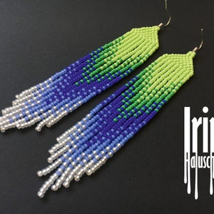 May include: A pair of long, beaded earrings with a gradient of colours, starting with silver, then light blue, dark blue, green, and ending with a bright lime green. The earrings are hanging from gold hooks.