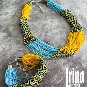 May include: A set of beaded jewelry featuring a necklace and bracelet. The necklace and bracelet are made of blue, yellow, and black beads. The beads are arranged in a geometric pattern. The necklace has a silver clasp. The bracelet has a silver clasp and a chain.